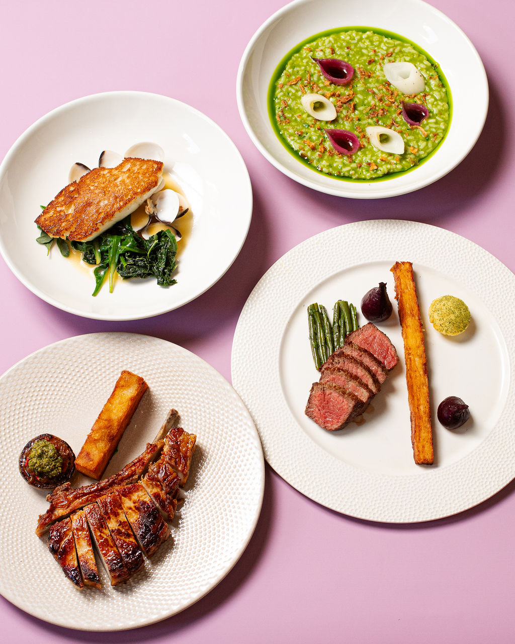 A spread of plated dishes on a pink studio backdrop