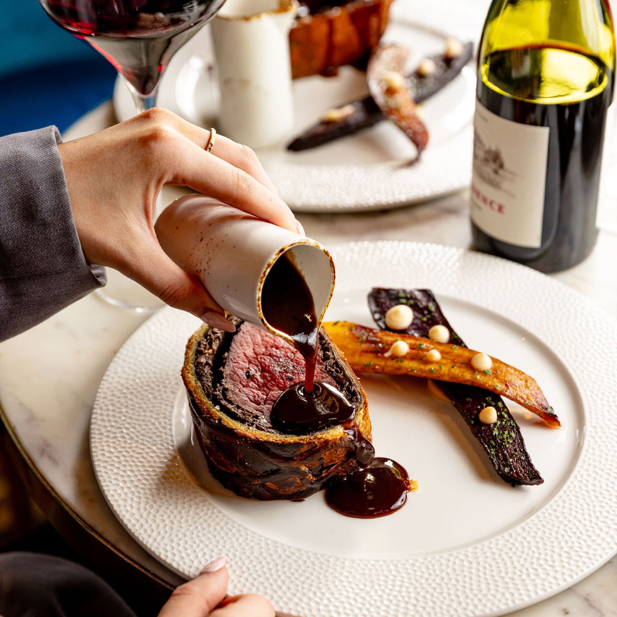 Red wine jus poured over the sliced Beef Wellington at the table