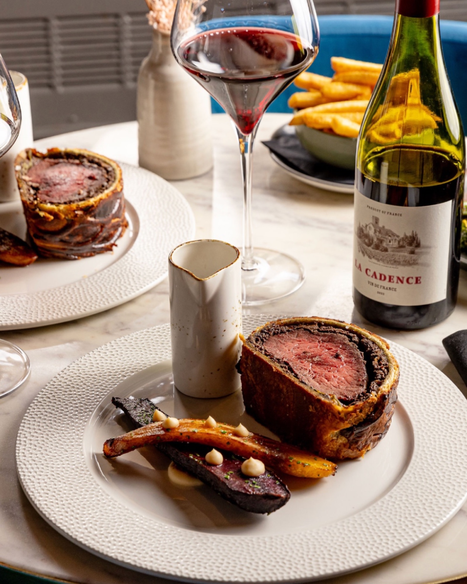 The Beef Wellington at the table with beef-fat carrots and a bottle of red